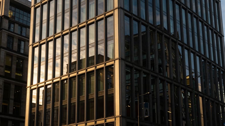 High-contrast editorial photograph of the exterior of 65 London Wall, sharp architectural angles, morning golden hour light reflecting off glass, deep navy and warm gold tones, 35mm