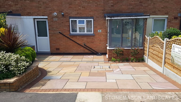 Colourful sandstone paving driveway and curved raised planter with colourful plants and flowers