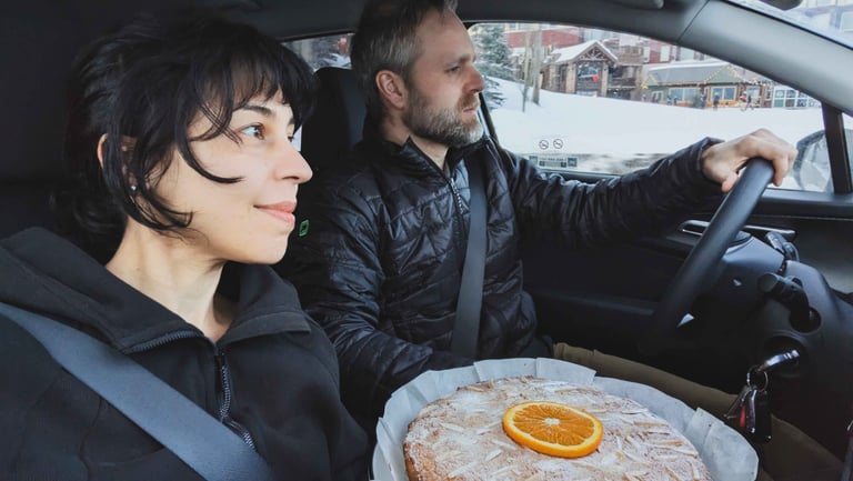 Two people sitting in a car with a homemade almond orange cake resting on a tray between them.