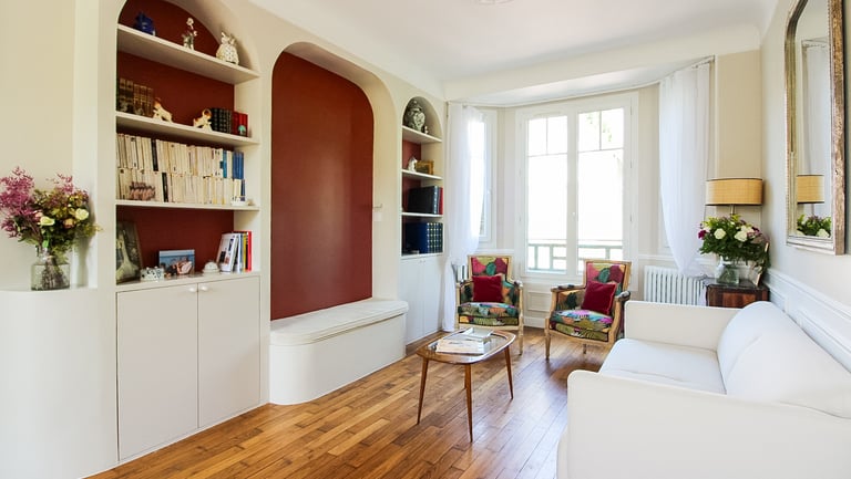 Salon cosy eclairé par un bow window avec une bibliothèque et une banquette intégrée
