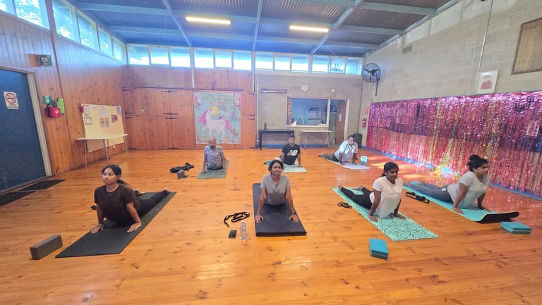 A group of people practicing cobra pose during a yoga class in a studio with wooden floors.
