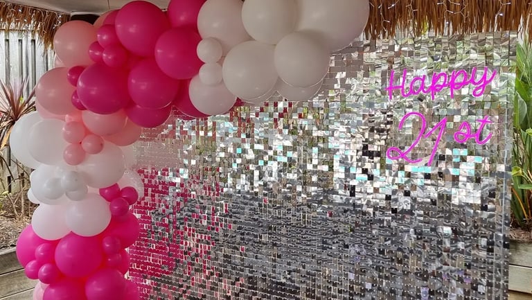 Silver shimmer wall with pink and white balloon garland and happy 21st neon sign.