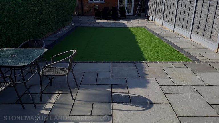 Fully paved grey sandstone patio with charcoal edging bocks and artificial grass lawn
