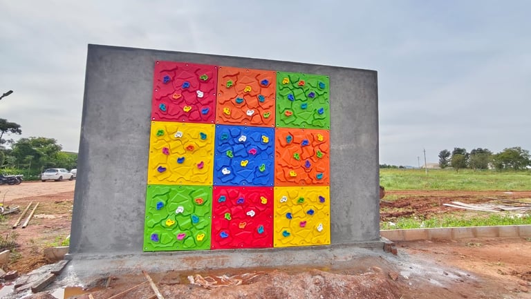 Colorful outdoor rock climbing wall for kids featuring multi-colored hand holds on a concrete structure.