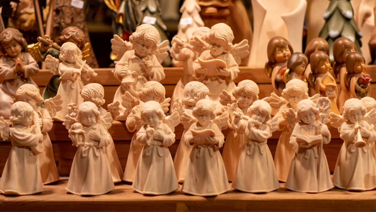 Handcrafted wooden angel figurines and musical cherub statues displayed at a traditional Christmas market.