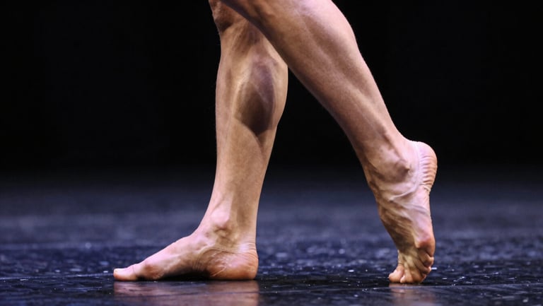 Close-up of a dancer's feet and lower legs in motion, stage floor visible, dramatic raking light from stage right, motion blur on the trailing foot, sharp focus on the planted foot, dark background
