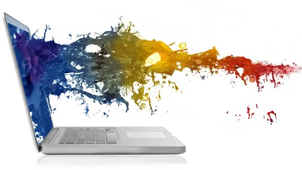 A laptop on a white background with a colorful splash of paint emerging from its screen.