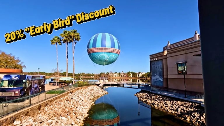 Hot air balloon over the lake at Disney Springs on a sunny day with shops and palm trees nearby.