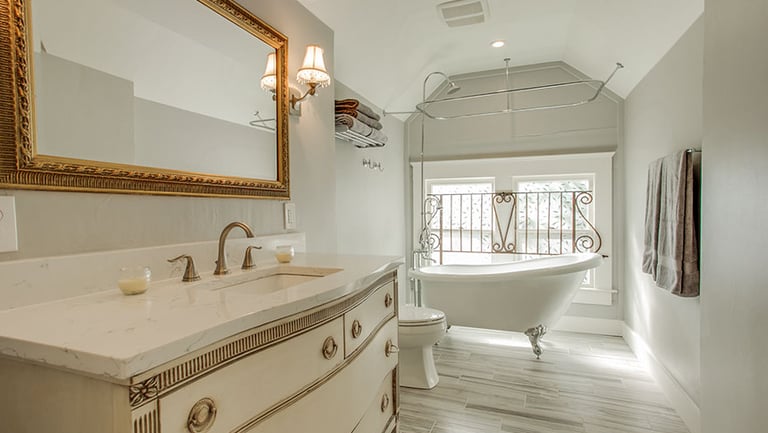 Elegant master bathroom with a vintage vanity, gold framed mirror, and clawfoot soaking tub.