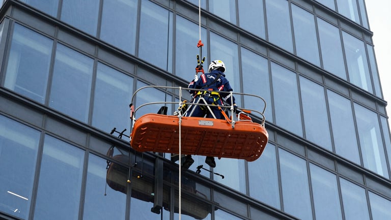 A heavy-duty rope suspended platform hanging securely against a modern glass skyscraper facade, crisp industrial photography, bright daylight, safety-orange accents, 35mm.