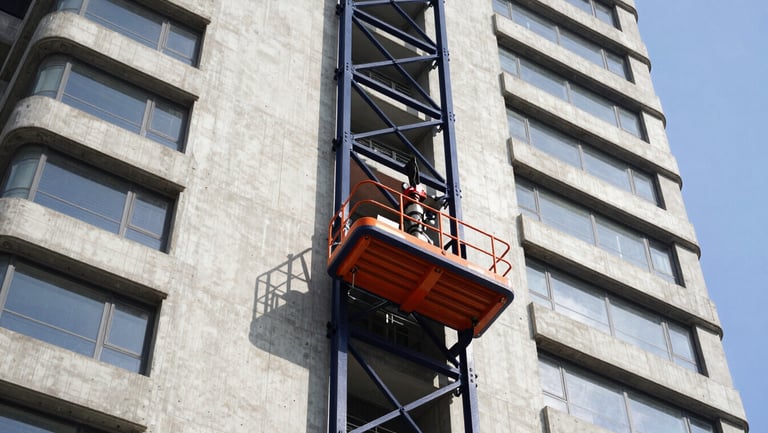 A high-capacity rack and pinion passenger hoist climbing the concrete side of a massive high-rise tower, bright daylight, navy blue steel frame, 35mm.
