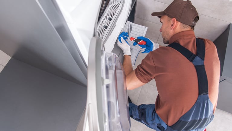a man in overalls and a hat, working on a refrigerator