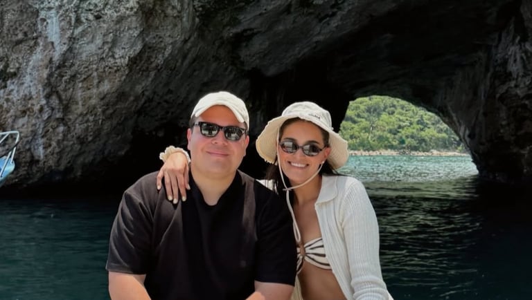 A couple sits on a boat in front of a sea cave archway during a summer vacation boat tour.