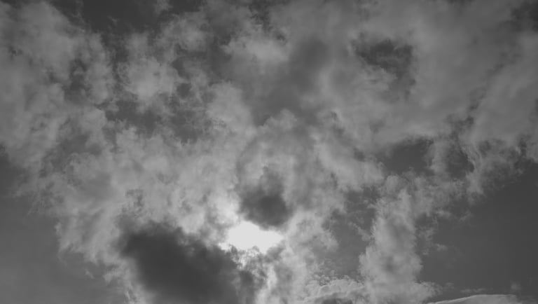 Cielo nublado en blanco y negro con la luz del sol entre las nubes.