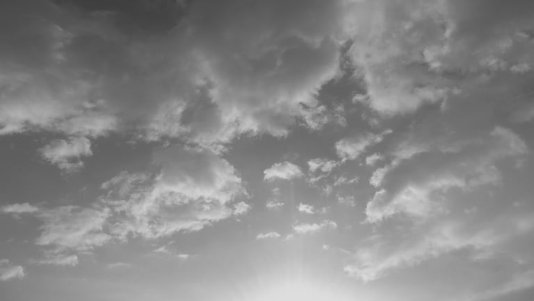 Cielo nublado en escala de grises con resplandor solar inferior.