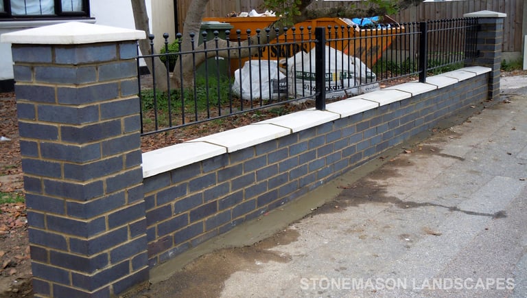 Blue perforated engineering brick wall with white coping, caps and black railings - Romford