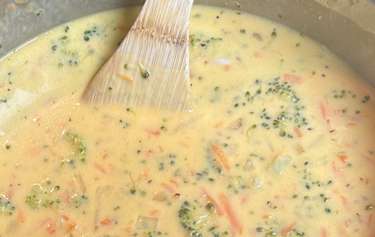 Broccoli Cheddar Soup in a pot with a wooden spoon sitting there.