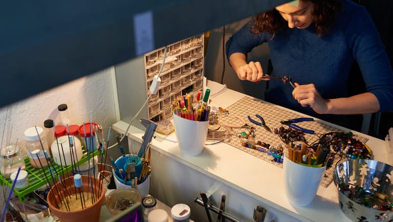 Creador de joyería usando alicates en un escritorio con cuentas de vidrio y materiales de artesanía 