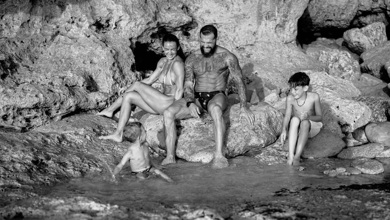 Family sitting together on coastal rocks during a candid family photography session at Dreamland Beach Bali.