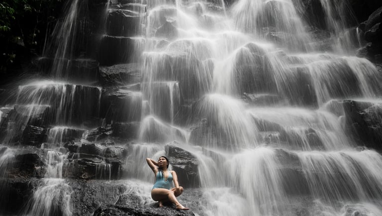 Wide portrait of woman sitting on rocks with waterfall at Kanto Lampo Bali