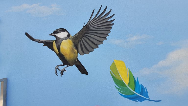 Fresque peinte sur une façade. Une mésange et une plume colorée s'envolent sur un ciel bleu.