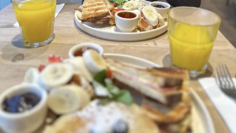 Assiettes de brunch avec pancakes, fruits, gaufres, confitures et verres de jus d’orange.