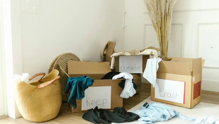 Home closet decluttering with cardboard boxes labeled keep, donate, and trash for organizing clothes.