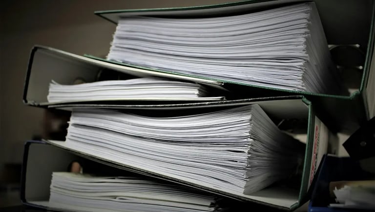 Stacked office ring binders overflowing with white paper documents for business organization and record keeping.