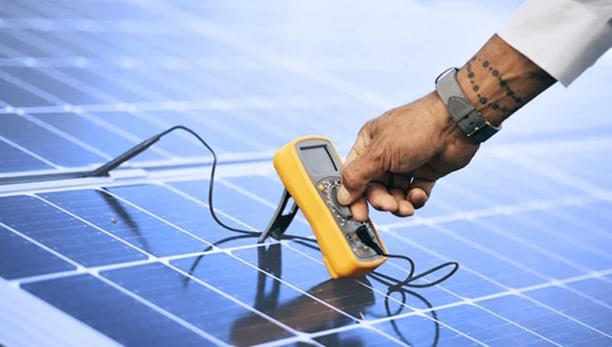 A technician uses a digital multimeter to test and maintain solar panels for efficient energy output.