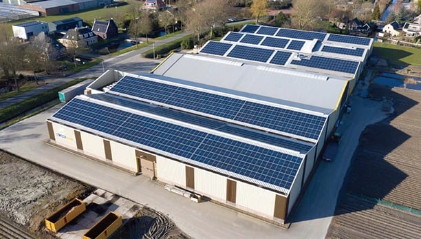 Aerial view of a large commercial warehouse roof covered in solar panel installations for renewable energy.