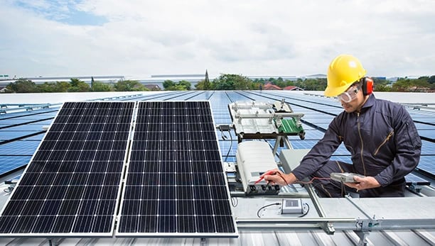 A solar technician in safety gear performs maintenance on industrial rooftop solar panels.