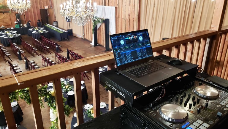 a dj booth with a laptop overlooking a wedding ceremony space from the balcony