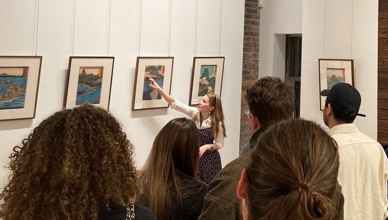 Madison pointing at a print while leading an exhibition tour for a large group