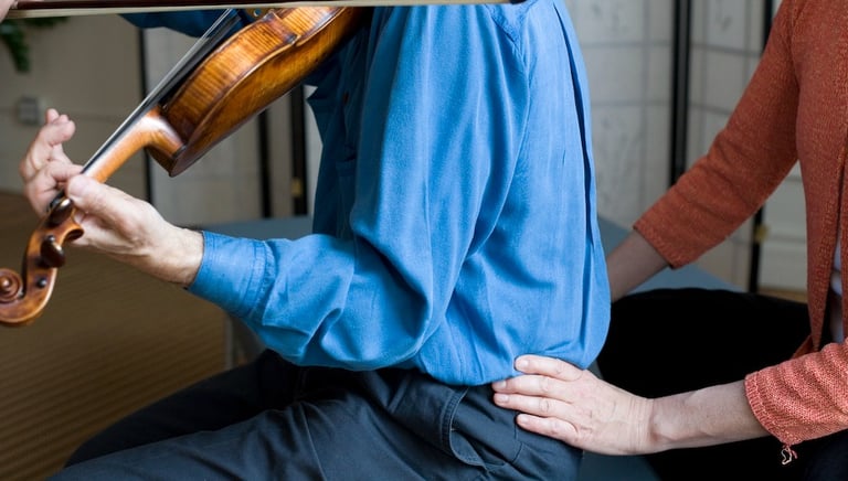 A feldenkrais teacher is helping a violinist find a better way of sitting