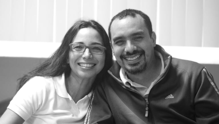 Un hombre y una mujer sentados uno junto al otro en un sofá, sonrientes miran la cámara