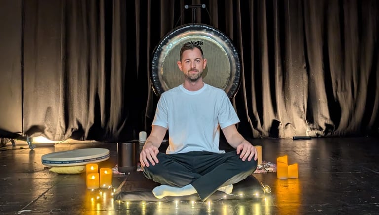 a man sitting in front of a gong leading a relaxing sound bath