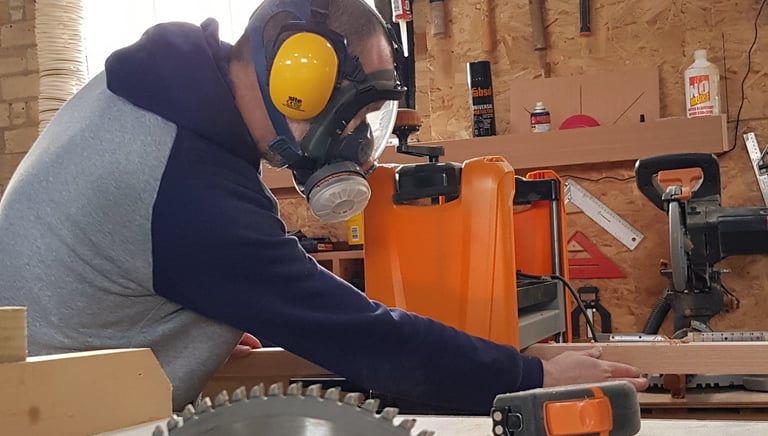 a man in a respirator mask and ear defenders in a workshop