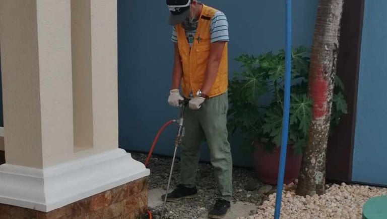Professional pest control technician performing termite soil treatment at a residential home foundation.