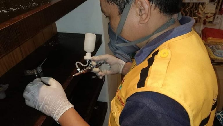 Professional pest control technician wearing a respirator mask and spraying pesticide in a wooden cabinet.
