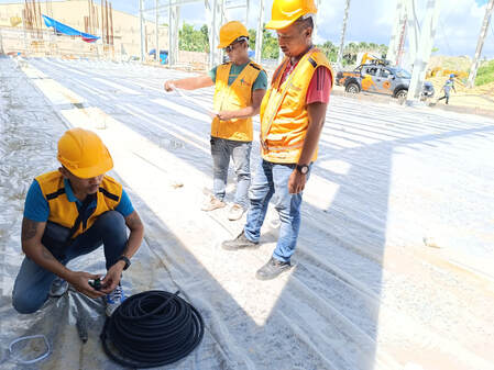 Construction workers in safety gear install a vapor barrier membrane on a building foundation site.