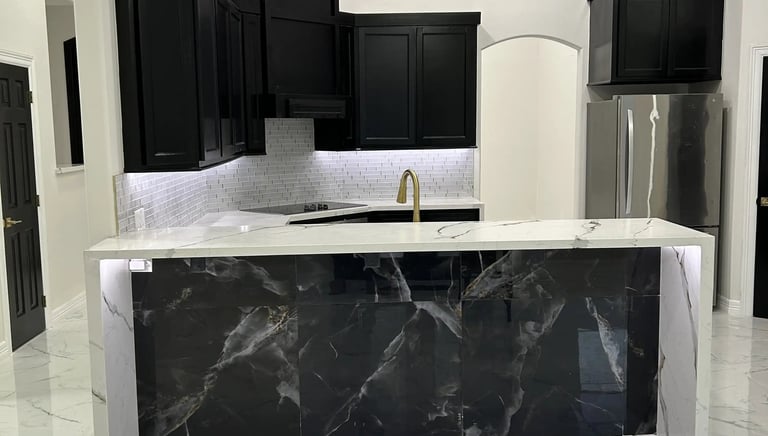 Modern luxury kitchen with black cabinets, white marble floors, and a dark marble waterfall island.