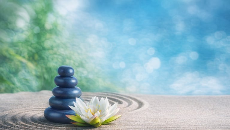 Balanced stack of blue stones beside a white lotus flower on raked sand in a peaceful Zen garden setting
