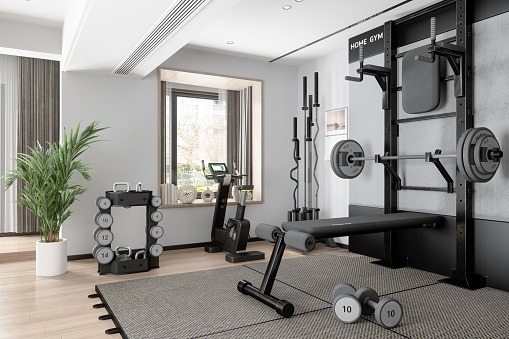 Home gym with bench, barbell, dumbbells, and kettlebells in a bright room with large windows