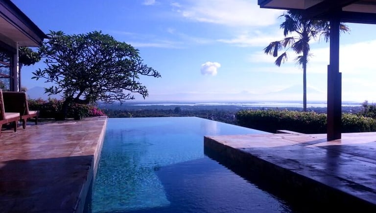 Luxurious infinity pool overlooking a tropical landscape with mountains, ocean, and clear blue sky in Bali.