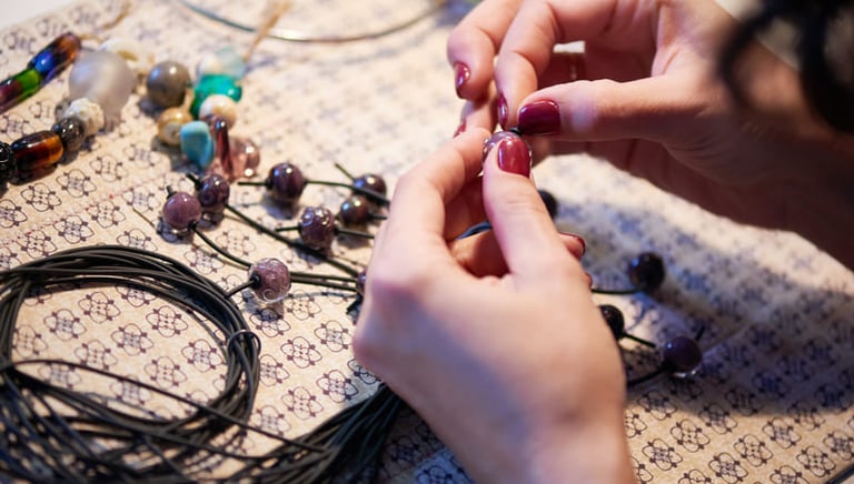 Acercamiento de manos realizando DIY con cuentas en hilo negro