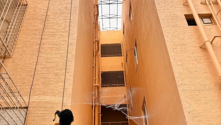 A professional installer rappels down a building to install white anti-bird netting in an apartment duct area.