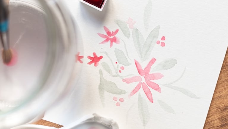 Fotografía que se centra en una ilustración de colores suaves de flores en acuarela se ve también la pastilla de color