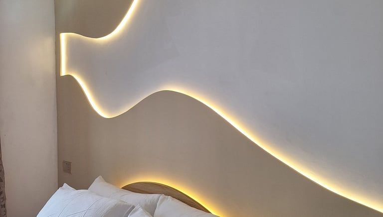 Modern bedroom featuring a minimalist headboard with warm LED wave lighting and white pillows.