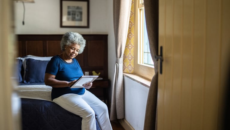Senior woman sitting on a bed looking back at a photo of a loved one with quiet reflection