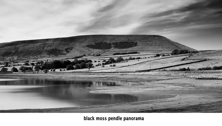 a black and white photo of pendle hill reflected in the waters of black moss reservoir